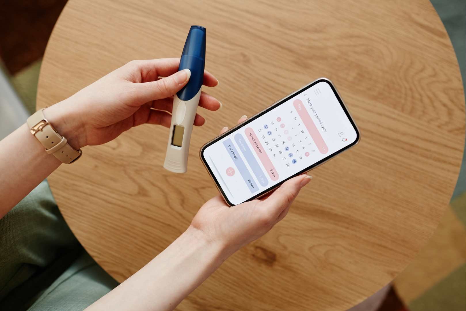 Photo of a pair of hands holding a pregnancy test and a phone, open on a calendar app