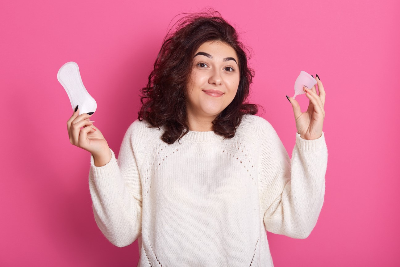Photo of woman holding a pad and a menstrual cup on a pink background