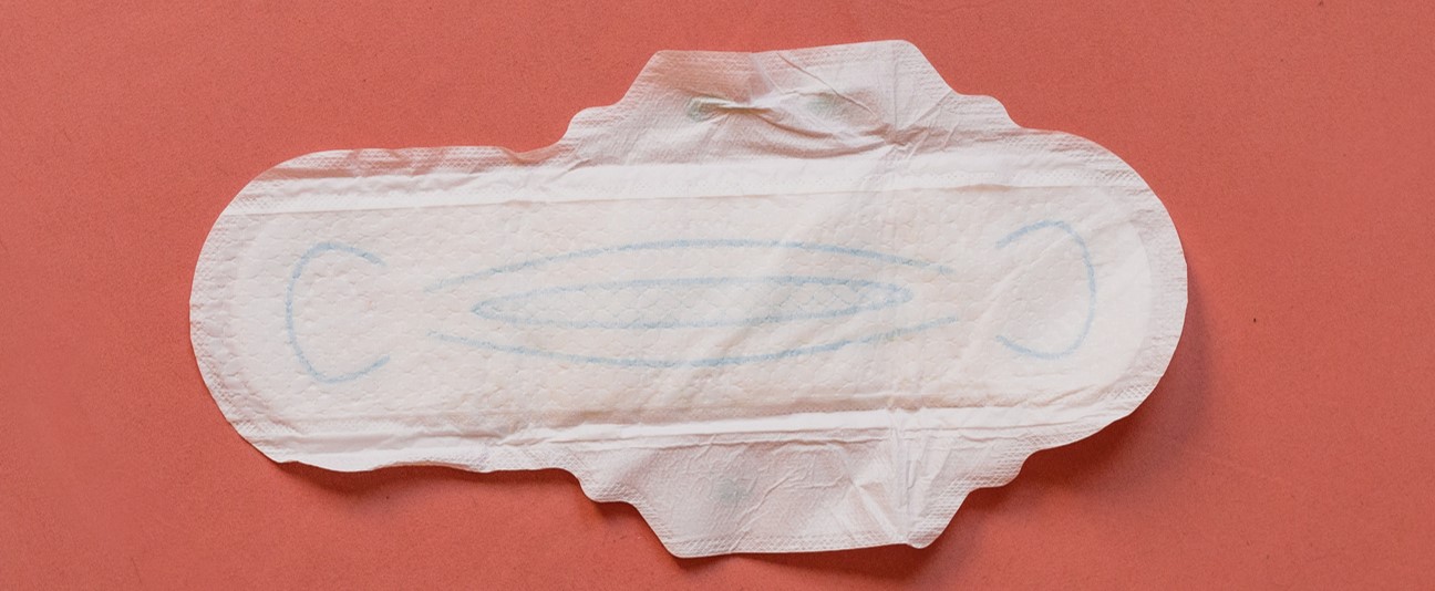 Photo of a white disposable period pad, unfolded on a dark pink background