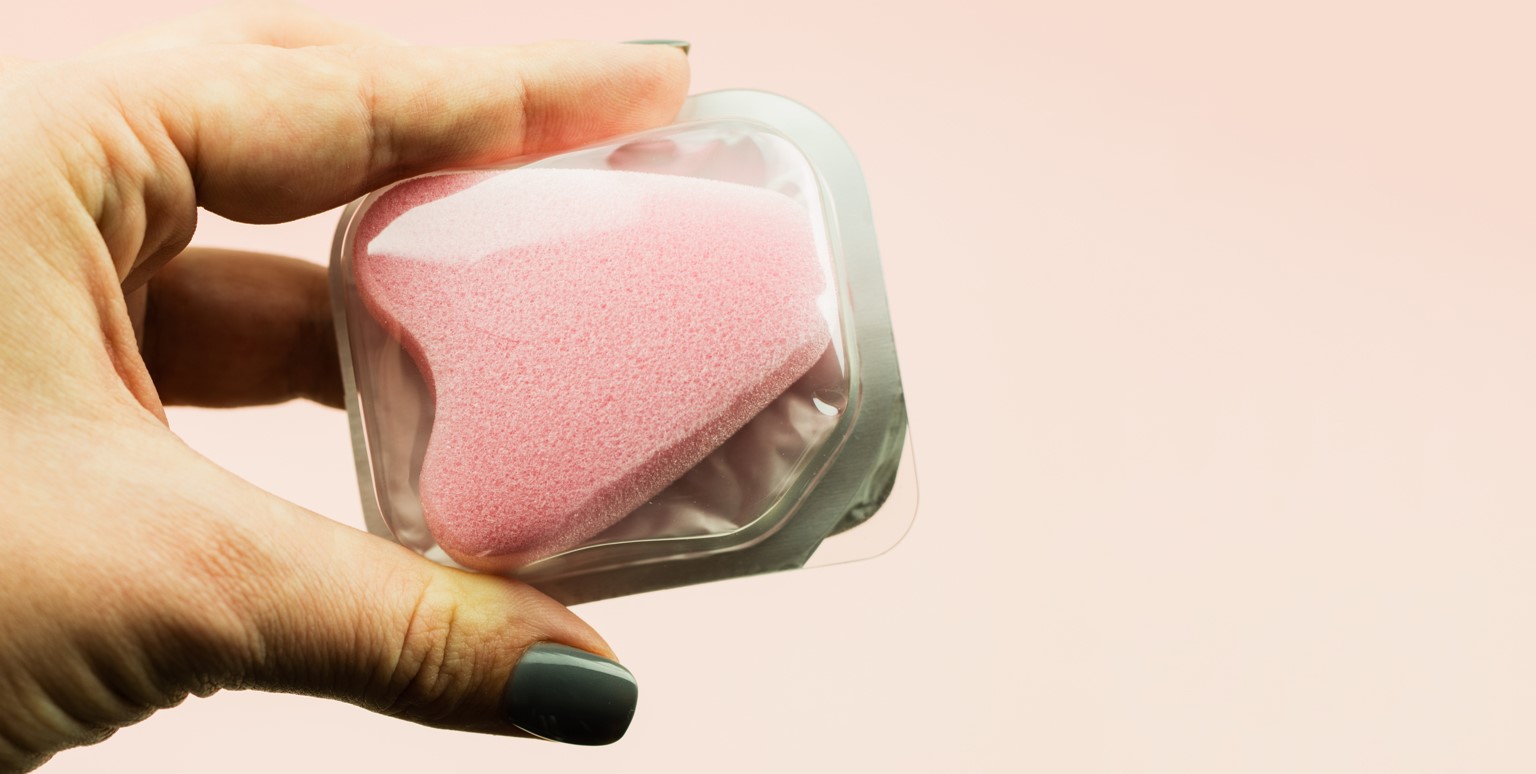 Photo of a hand holding a pink menstrual sponge in plastic wrapping