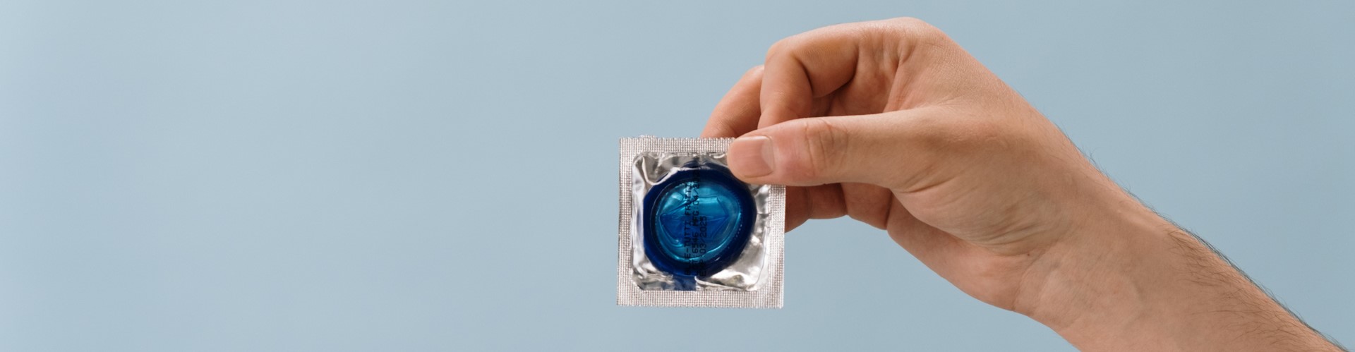 Photo of a hand holding a condom on a light blue background