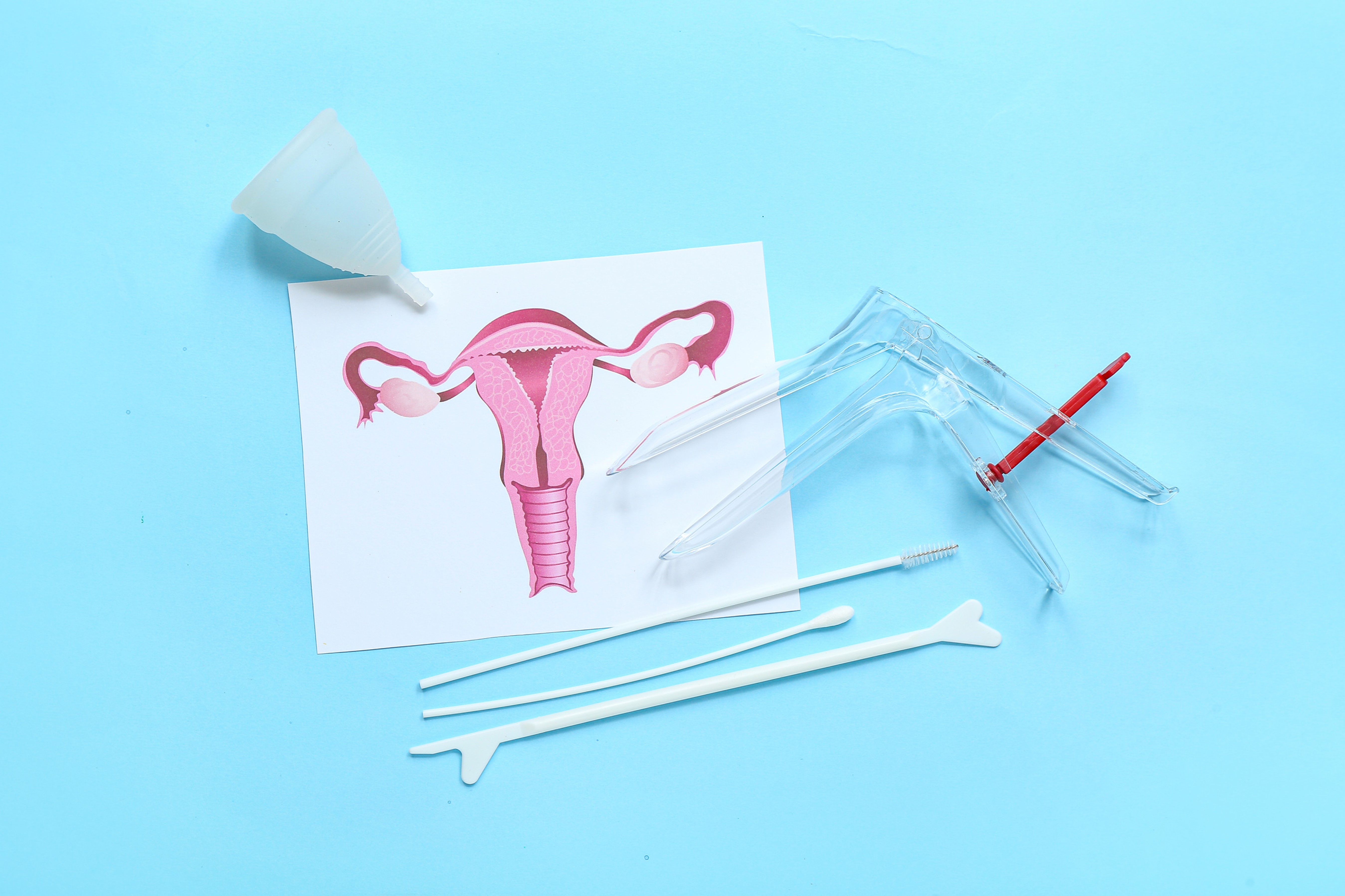 Photo of a uterus diagram, speculum, vaginal swabs and a menstrual cup on a blue background