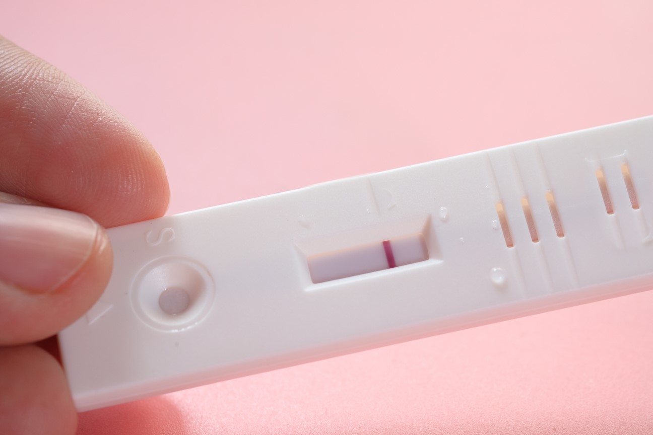 Photo of a hand holding a positive pregnancy test on a pink background