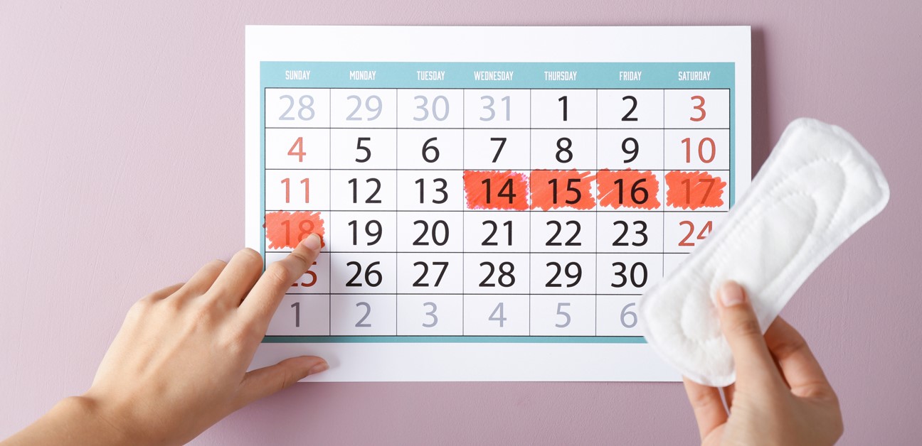 Photo of calendar and person's hand holding a menstrual pad