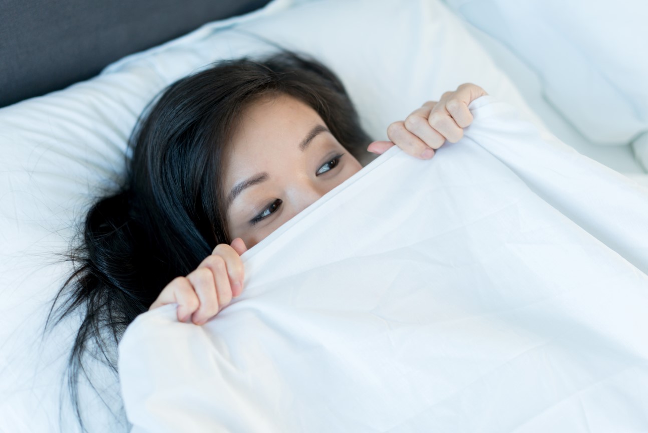 Photo of a scared woman in bed under sheets
