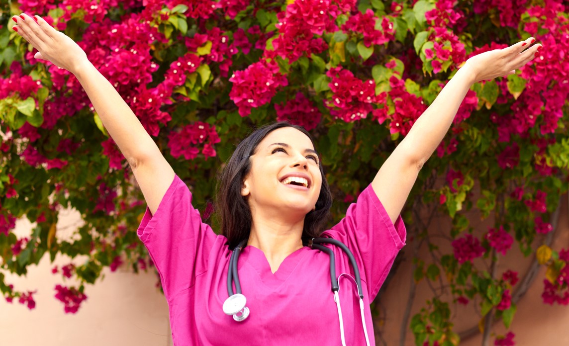 Photo of a woman in pink scrubs with her arms in the air, smiling