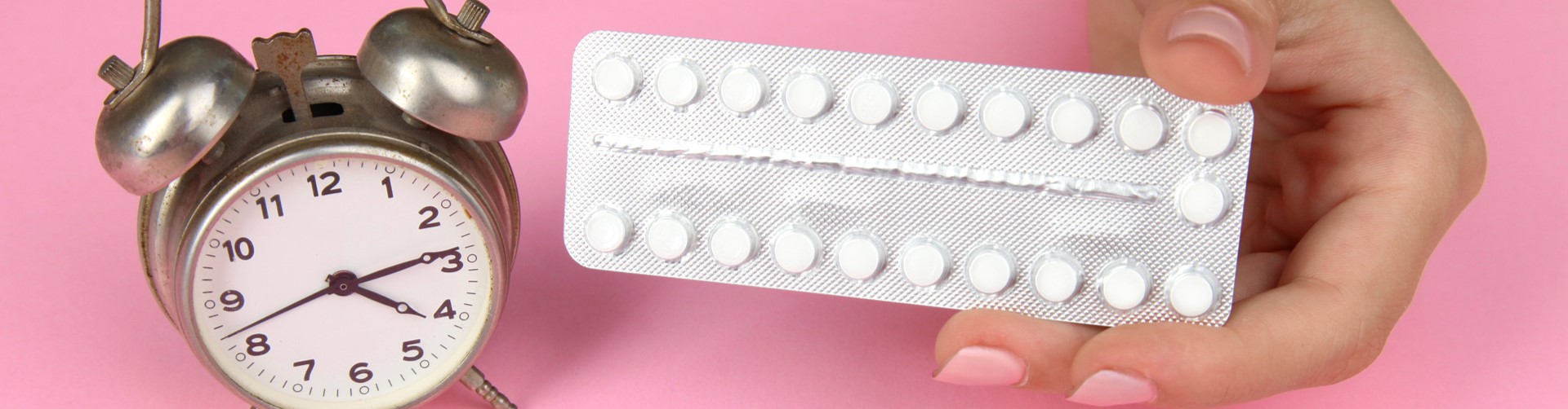 Photo of a contraceptive pill packet and a silver clock on a pink background