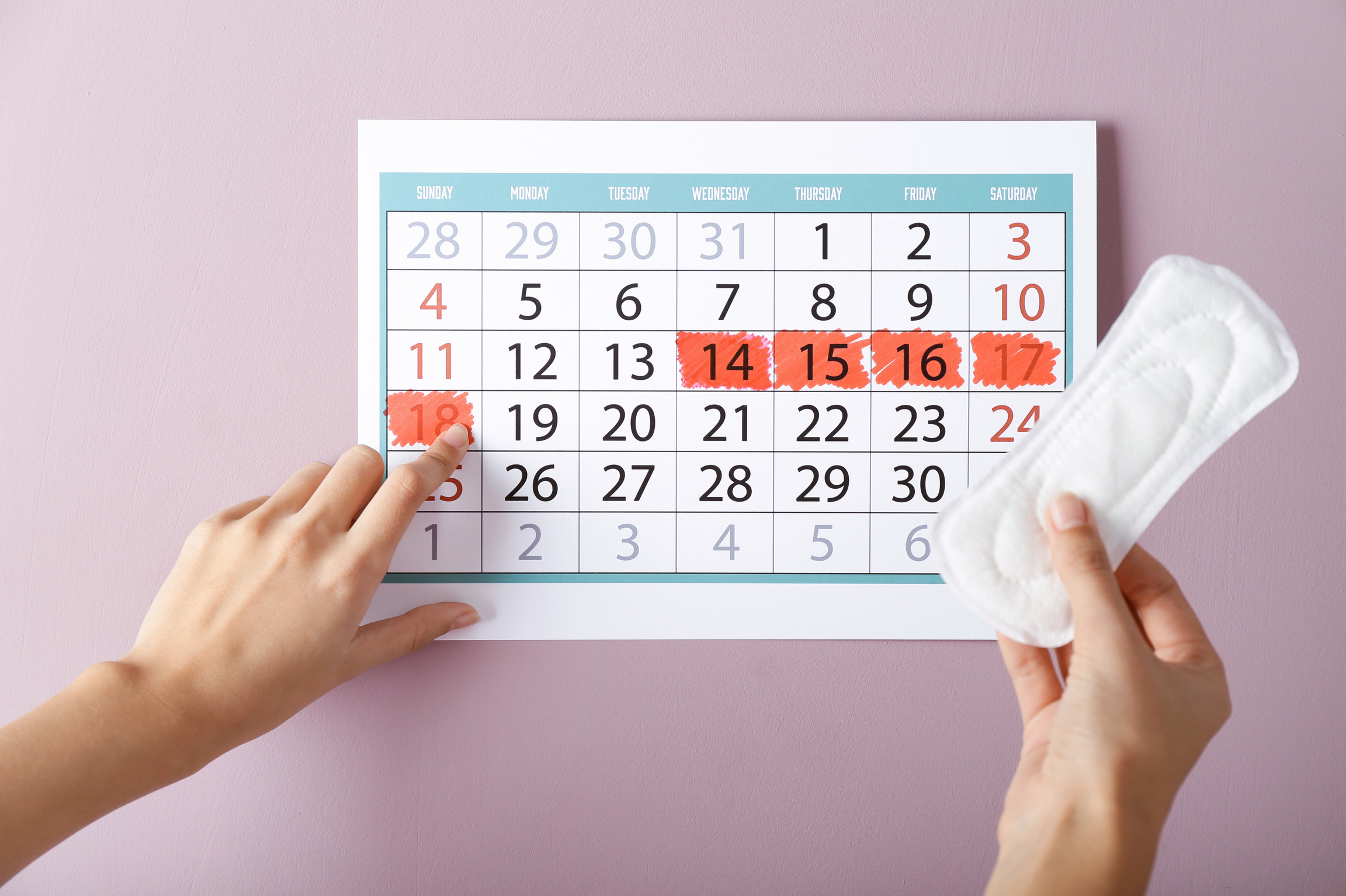 Photo of a calendar and hand holding a pill packet on a pink background