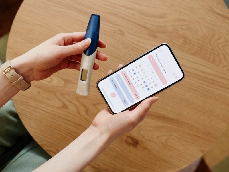 Photo of a pair of hands holding a pregnancy test and a phone, open on a calendar app