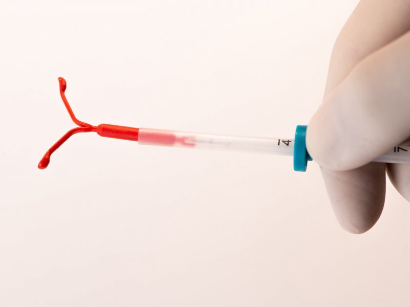 photo of a gloved hand holding a red IUD