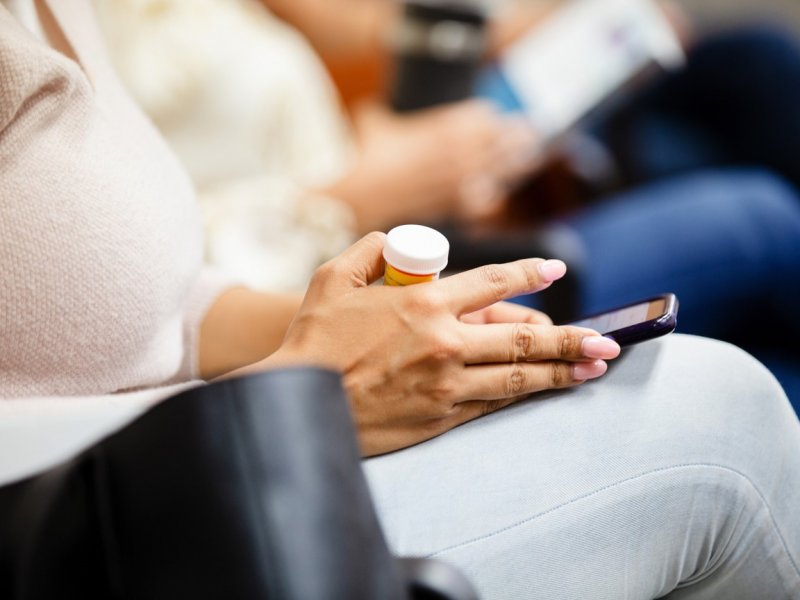 Photo of a person's hands holding an orange medication container and using their phone