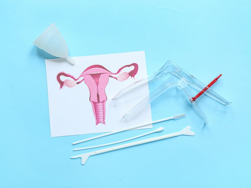 Photo of a uterus diagram, speculum, vaginal swabs and a menstrual cup on a blue background