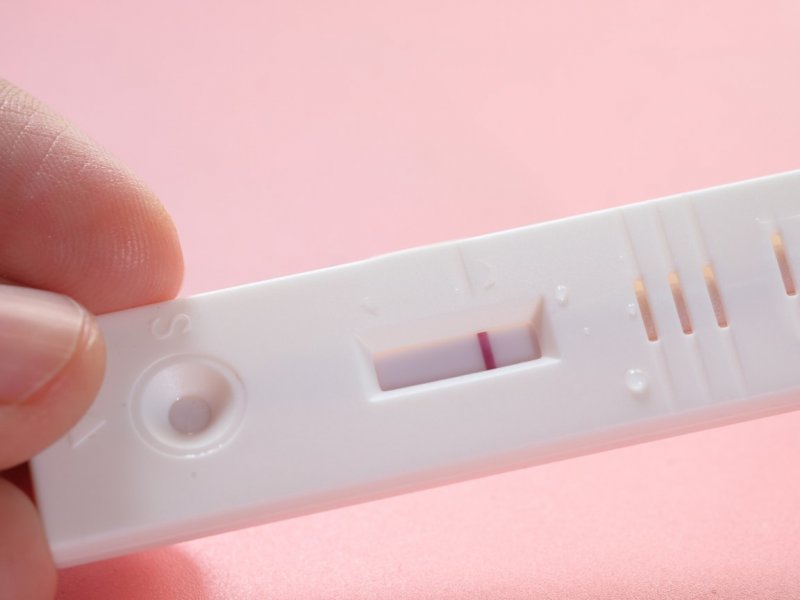 Photo of a hand holding a positive pregnancy test on a pink background