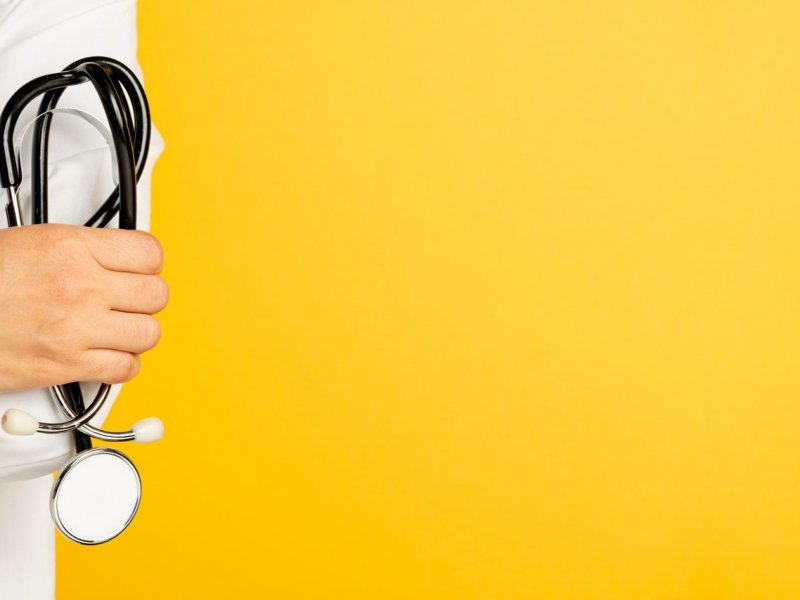 Photo of a doctor holding a stethoscope on a yellow background