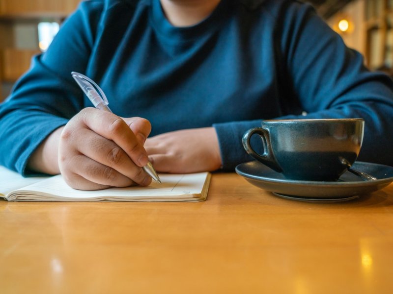 Photo of a tan hand writing in a diary