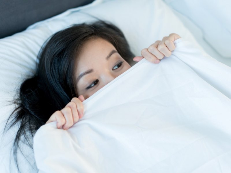 Photo of a scared woman in bed under sheets