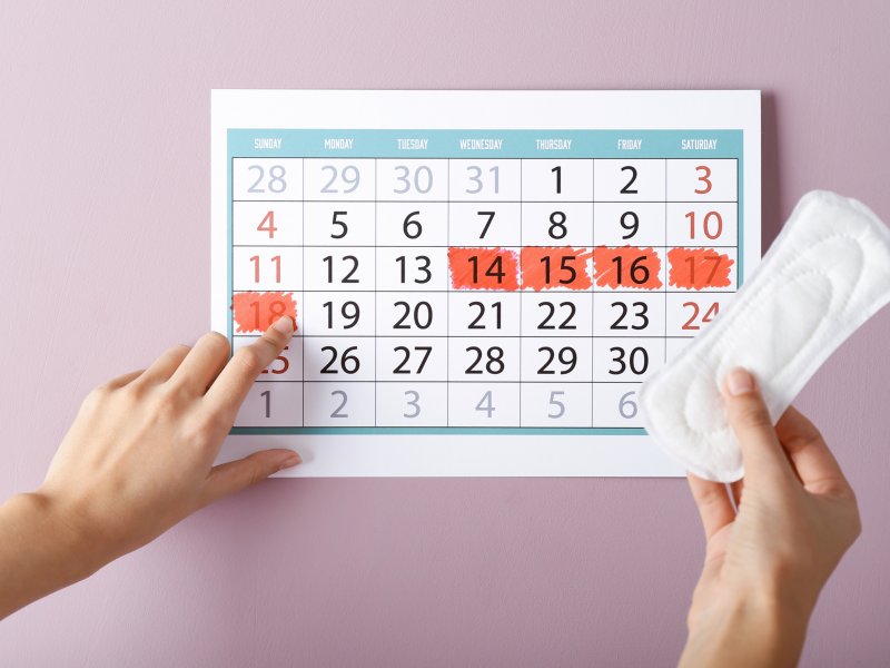 Photo of a calendar and hand holding a pill packet on a pink background