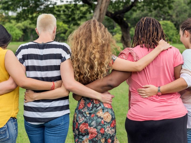 Photograph of five people with their arms around each others' backs