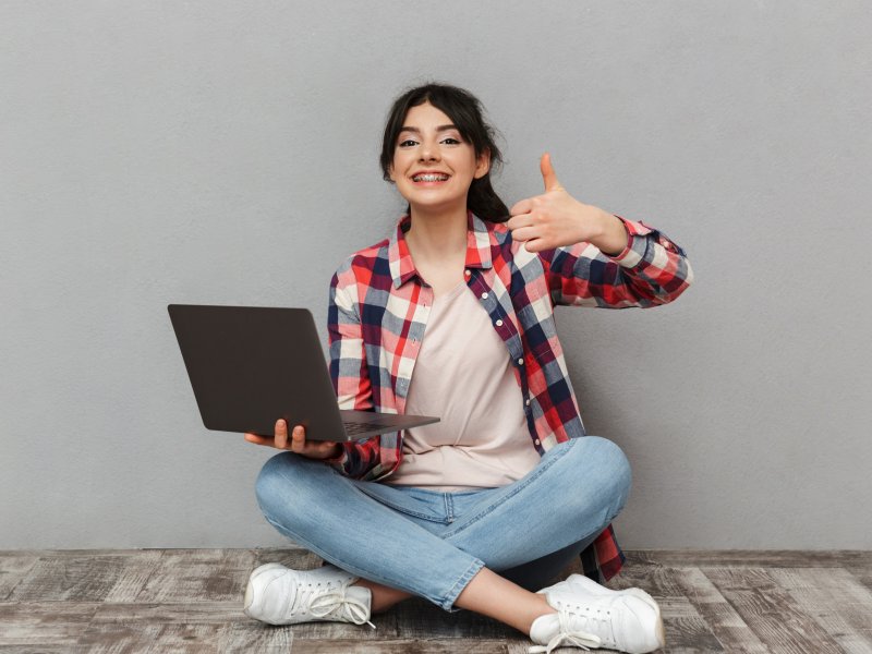 Photo of girl with braces sitting cross legged with a laptop